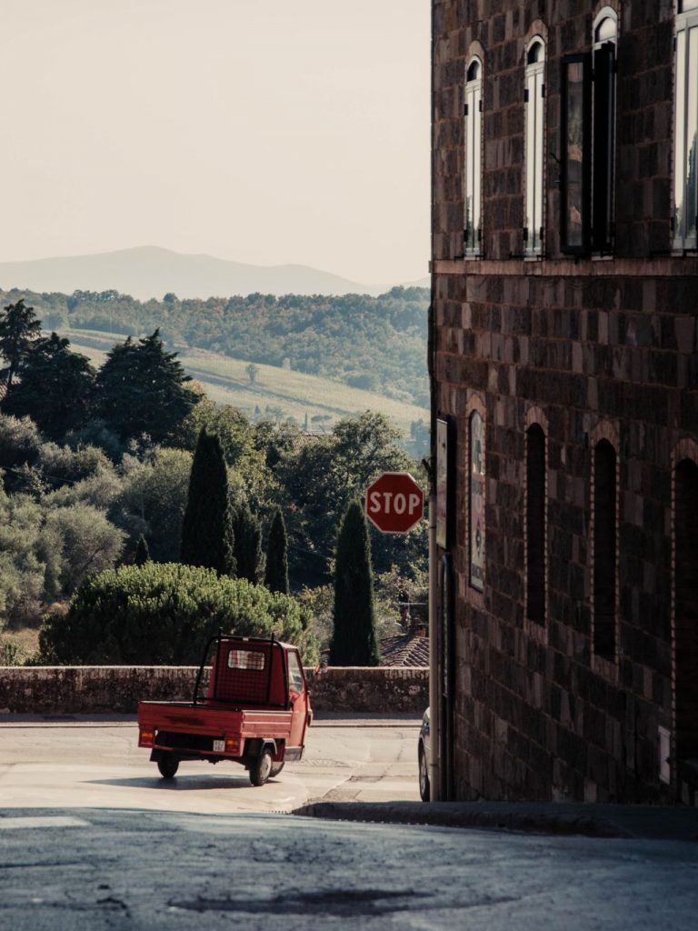 Eine Ape knattert über die kurvige Landstraße in der Hügellandschaft der Toskana - Roadtrip Momente